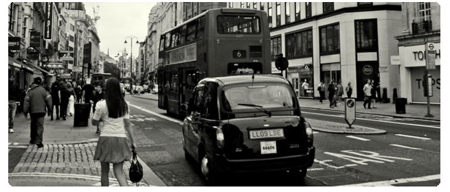 Image of a car driving down a busy street in the United Kingdom. Driving in the UK can be confusing. Follow these tips for safer driving.